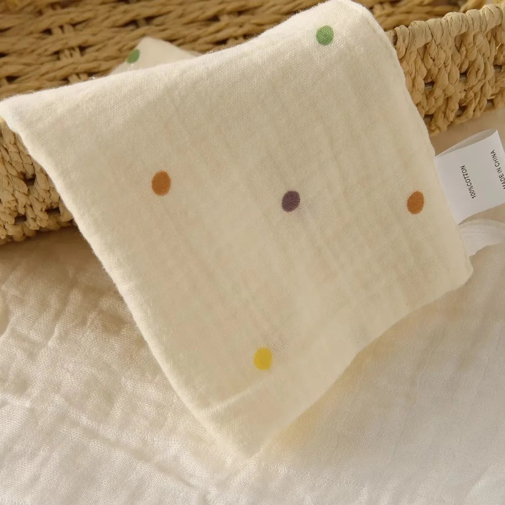 Soft white 100% cotton gauze baby towel with colorful polka dots, folded in a woven basket.