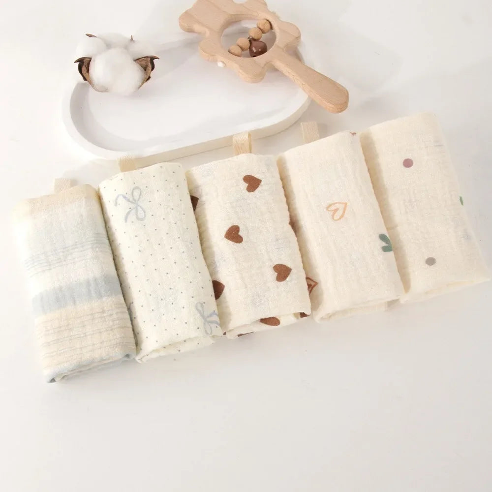Five rolled natural cotton gauze baby towels with various patterns, including hearts and dots.