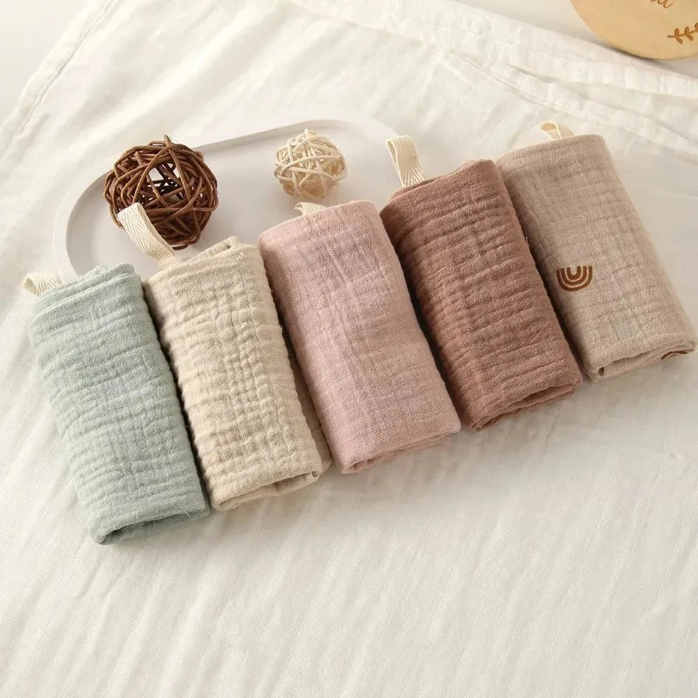 Soft cotton gauze baby towels in pastel shades: light blue, cream, pink, brown, and beige.
