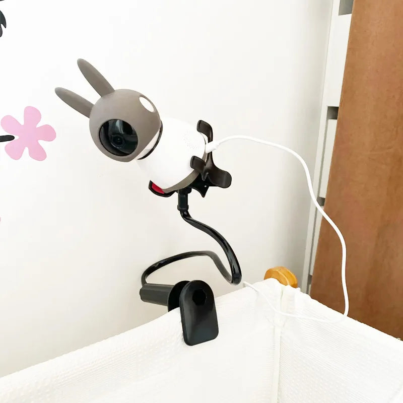 Flexible baby monitor holder with a black gooseneck arm, clamped to a white crib, featuring a cute gray and white monitor.
