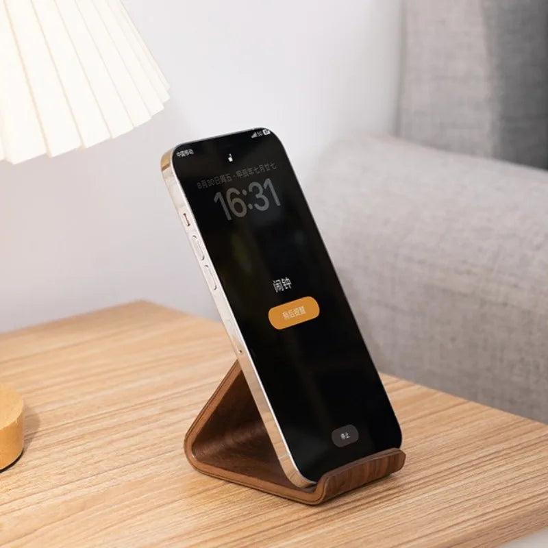 Dark walnut wood phone stand with a minimalist design, holding a silver smartphone on a light wooden table.