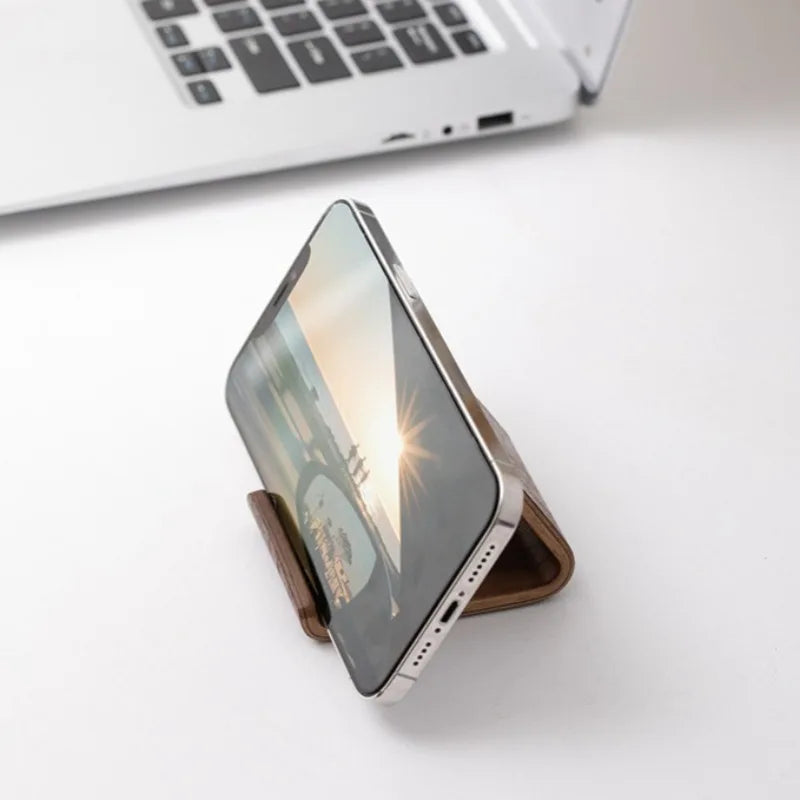 Minimalist dark walnut wood phone stand holding a smartphone horizontally on a white desk.