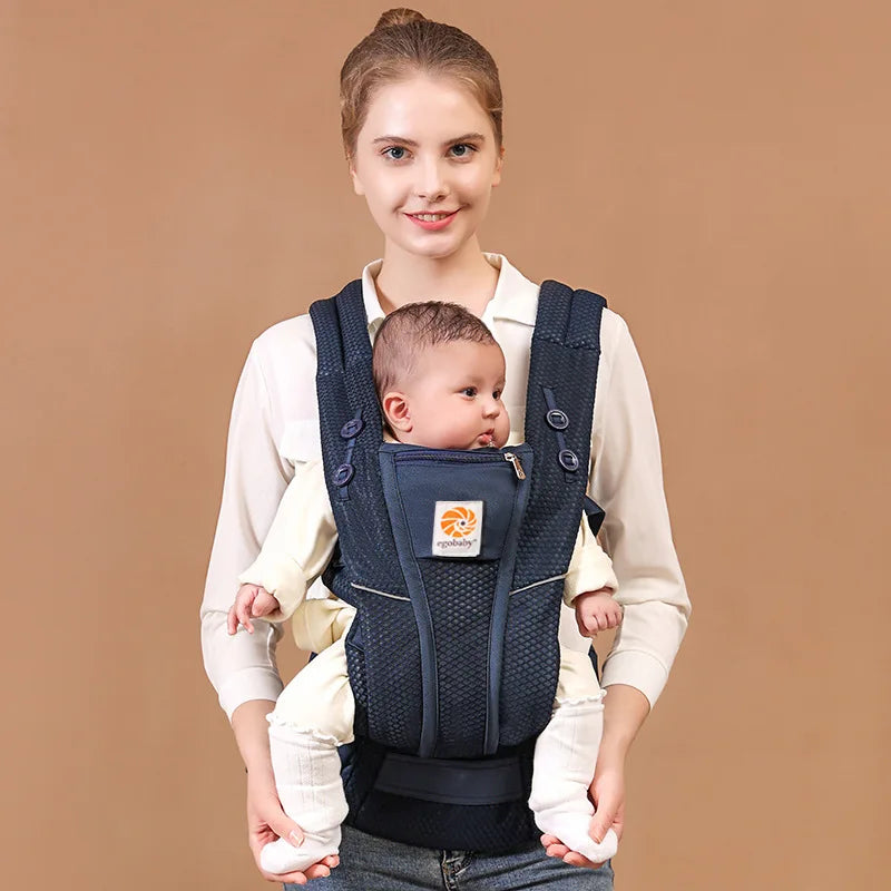 Woman smiling, wearing a navy blue ergonomic baby carrier with a baby facing forward.