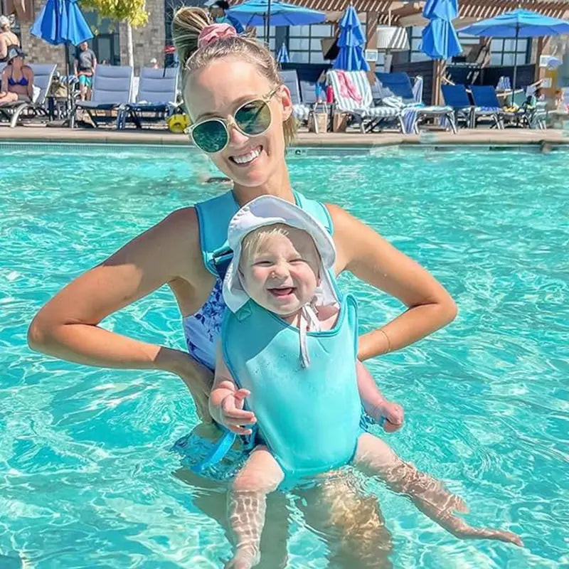 Woman and baby in a turquoise ergonomic pool baby carrier, smiling in a swimming pool.