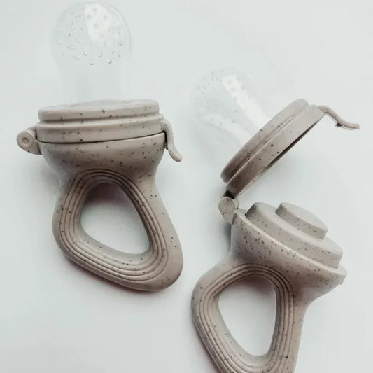 Two speckled beige baby fruit feeders with clear silicone nipples, one closed and one open.
