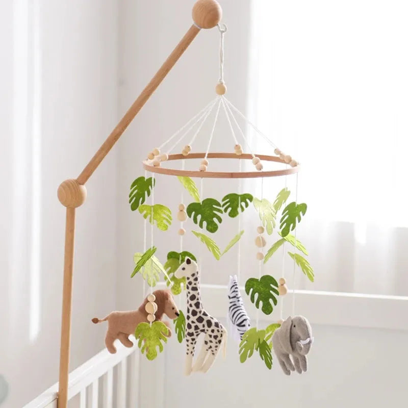 Wooden crib mobile with felt safari animals and green leaves, hanging over a white crib.