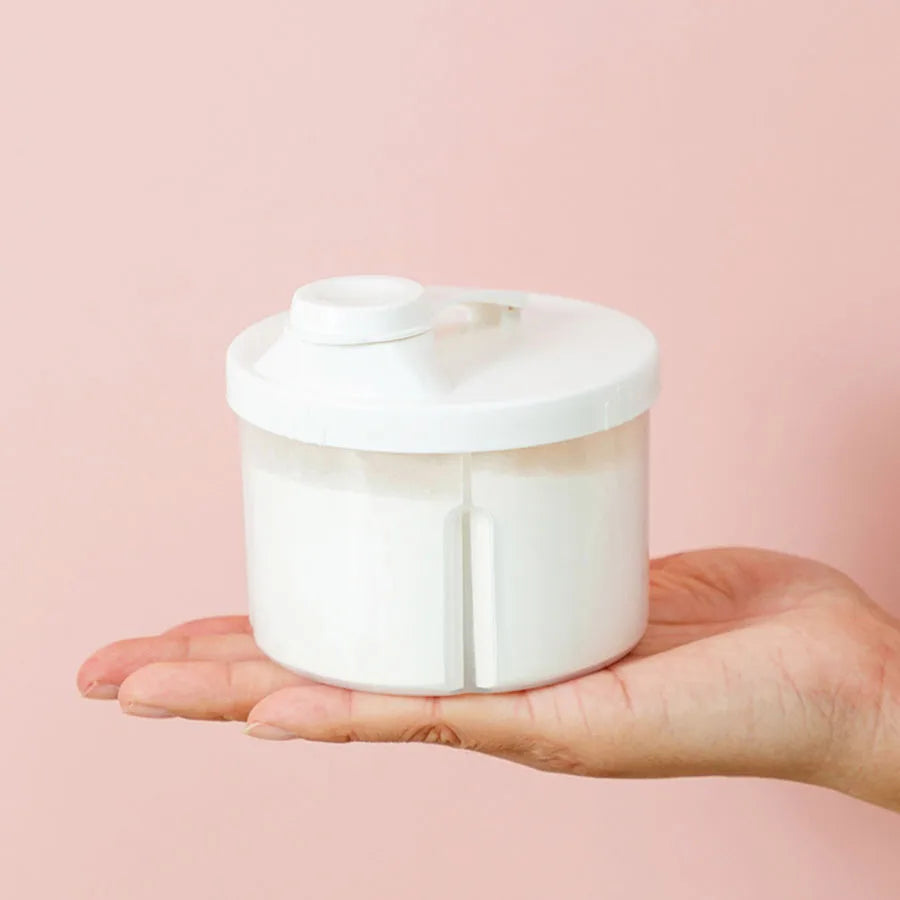 White 4-compartment portable baby formula and food storage container held in a hand.