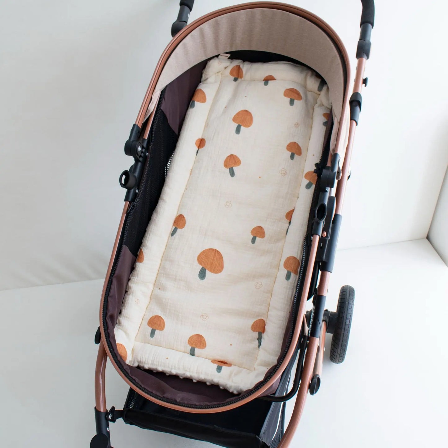 Soft beige cotton stroller cushion with orange mushroom print, nestled in a rose gold stroller.