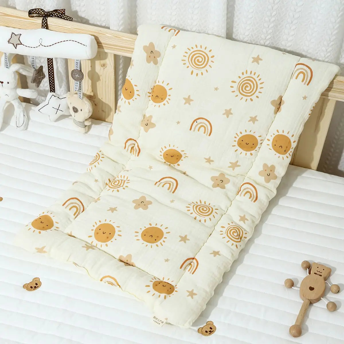 Soft cream baby stroller cushion with sun, rainbow, and star patterns, on a white crib mattress.