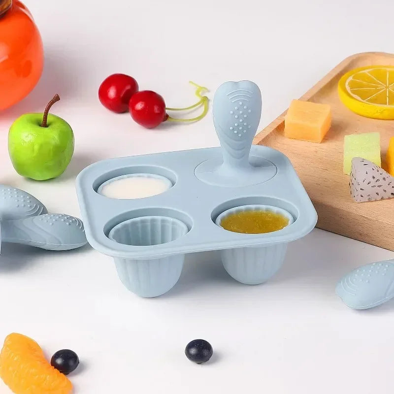 Light blue silicone baby fruit feeder with four compartments, two filled with purees, on a white surface.