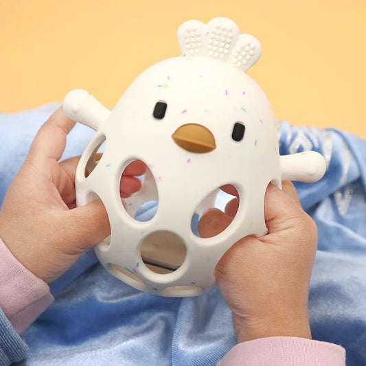 White silicone chicken teether with colorful sprinkles, held by baby's hands.