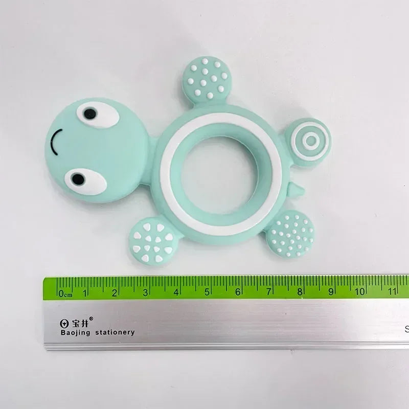 Mint green silicone turtle baby teether with white accents, textured feet, and a central ring for easy grip.