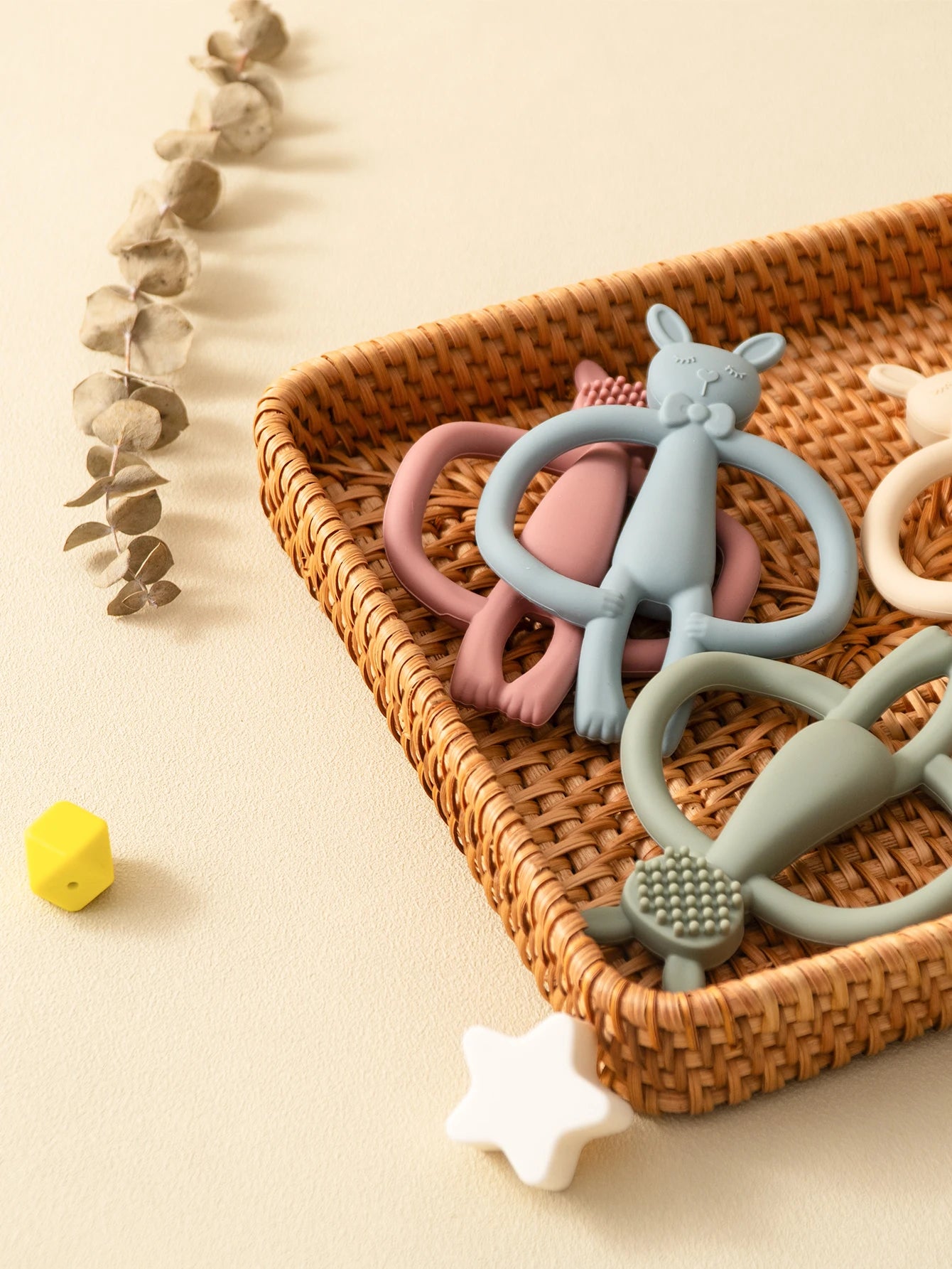 Soft silicone rabbit teethers in pink, blue, sage, and cream in a woven basket.