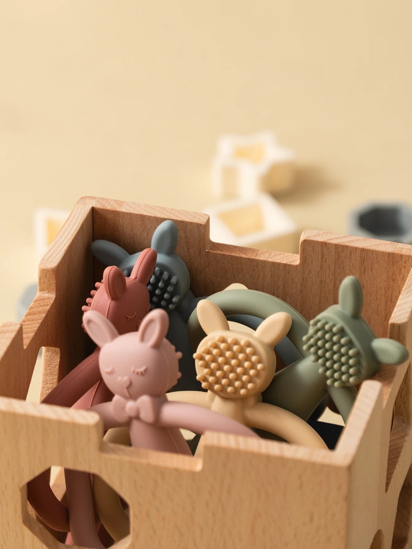 Soft silicone bunny teethers in various pastel colors, displayed in a wooden toy cart.