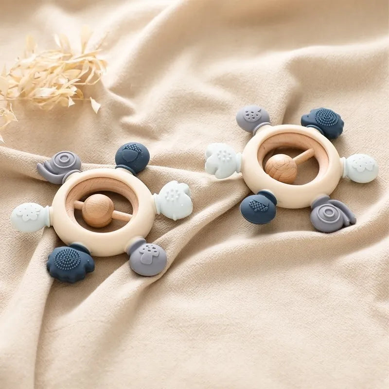 Two Montessori forest-themed soft silicone and wood baby teethers with various textured shapes.