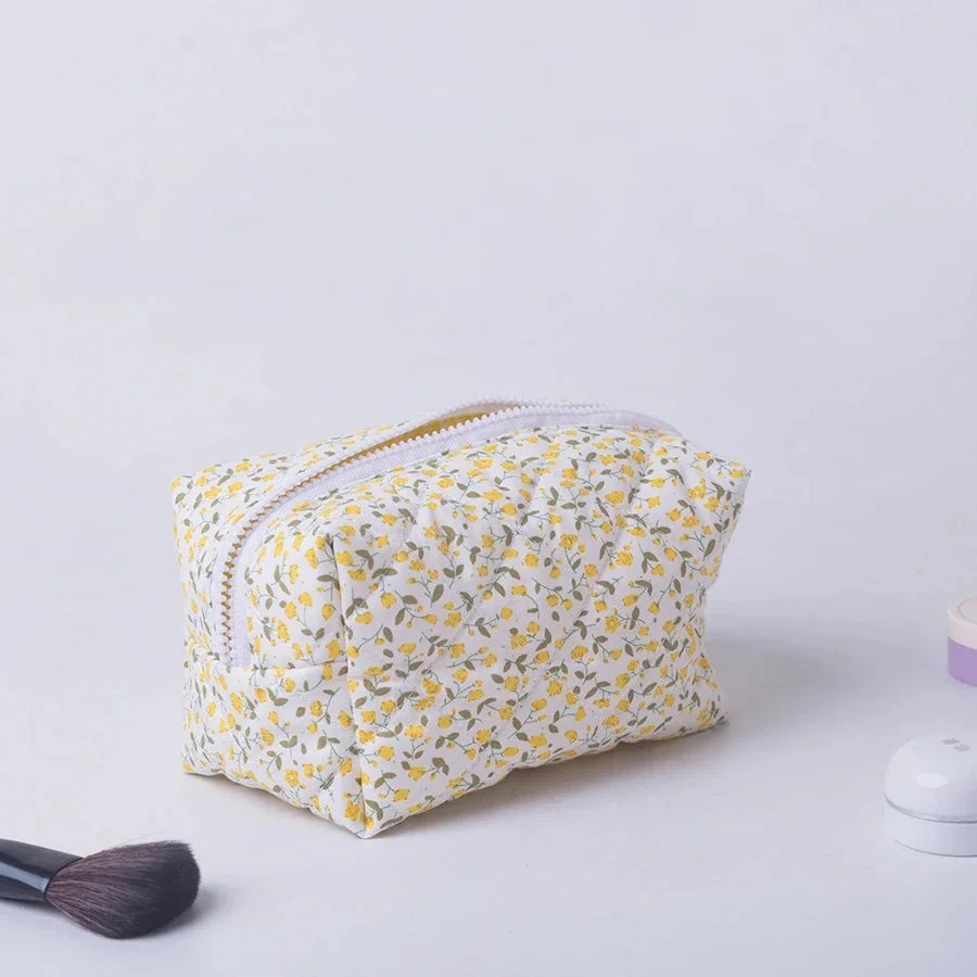 Padded floral makeup bag with yellow flowers, white zipper, and quilted polyester fabric.