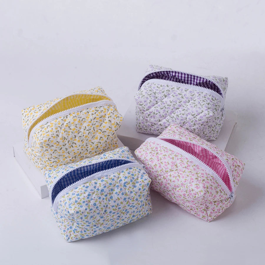 Four quilted floral makeup bags in yellow, purple, blue, and pink with zipper closures.