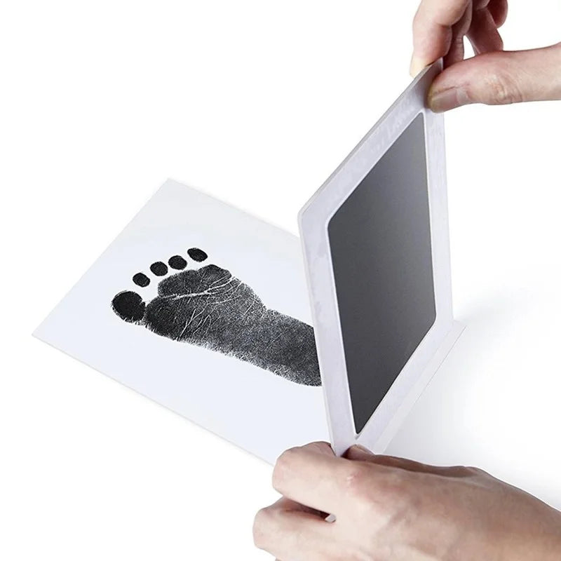 Hands holding a white, non-contact ink pad above a paper with a black baby footprint.
