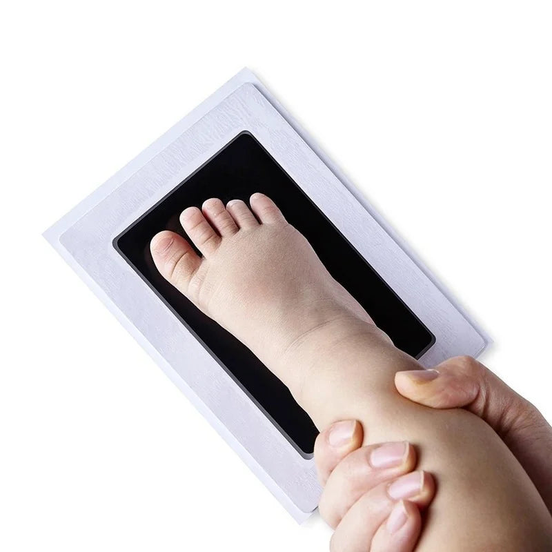 Baby's foot being pressed onto a white and black no-ink print kit for a safe, mess-free footprint.