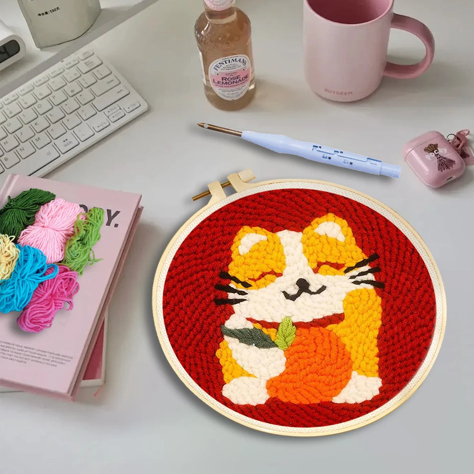 Punch needle embroidery kit with a cute cat holding a pumpkin design on red fabric in a wooden hoop.