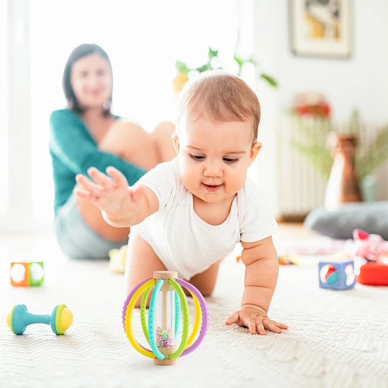 Baby crawling towards a wooden rain drum rattle with colorful silicone rings and a mother in the background.