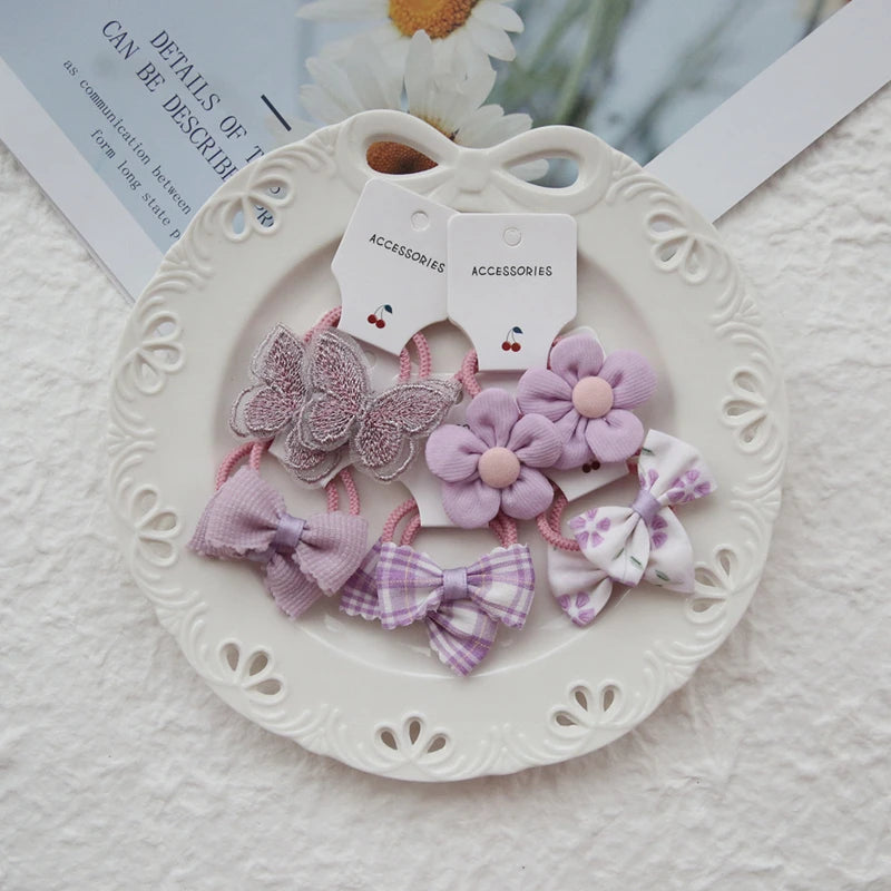 Set of 10 girls' purple floral and bow elastic hair ties on a white plate.