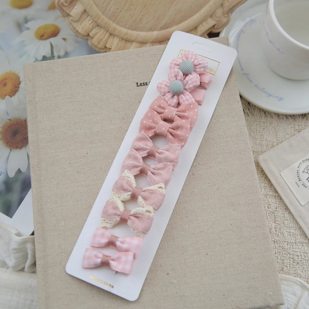 Set of 10 pink fabric bow and flower hair clips for babies and girls, on a book.