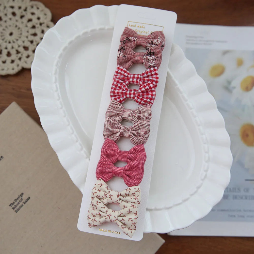Set of 10 fabric bow hair clips for babies and girls, in pink, red, and cream patterns.
