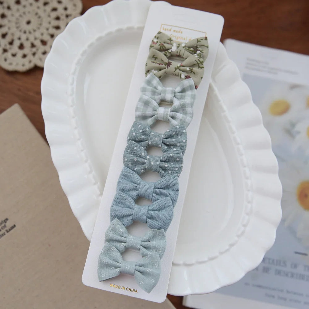 Set of 10 baby girl hair clips with fabric bows in green floral, plaid, polka dot, and solid blue.