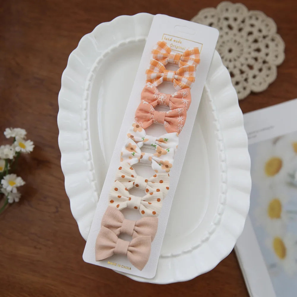 Set of 10 baby girl hair clips with fabric bows in orange, peach, floral, polka dot, and solid beige.