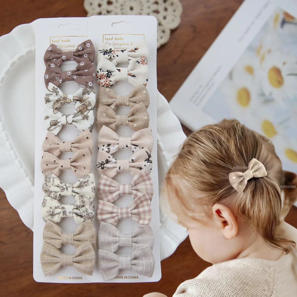 Set of 10 handmade fabric bow hair clips for babies and girls in neutral colors and patterns.