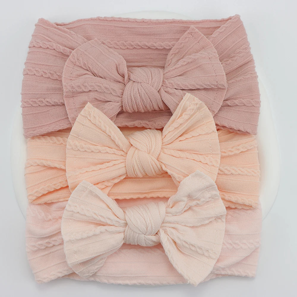 Set of 3 soft, flexible nylon baby headbands with bows in pink and peach shades.
