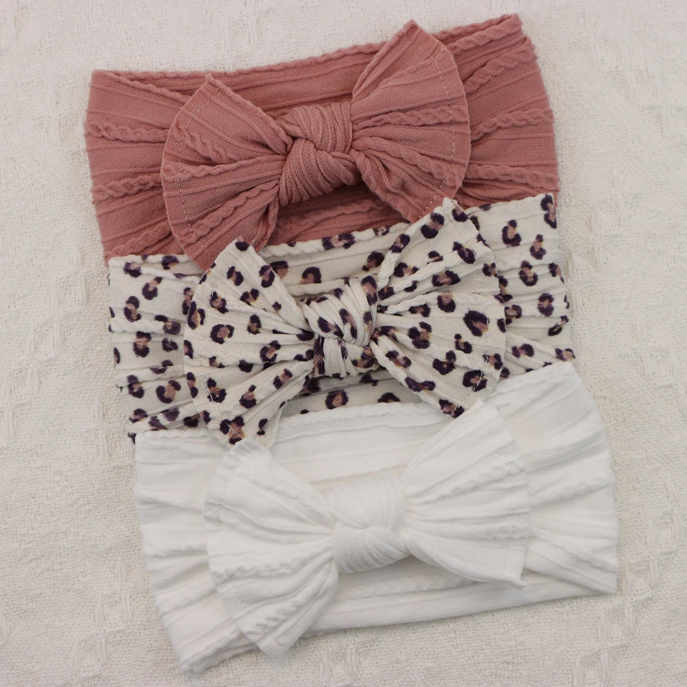 Set of 3 soft nylon baby headbands: pink ribbed, white leopard print, and white ribbed with bows.