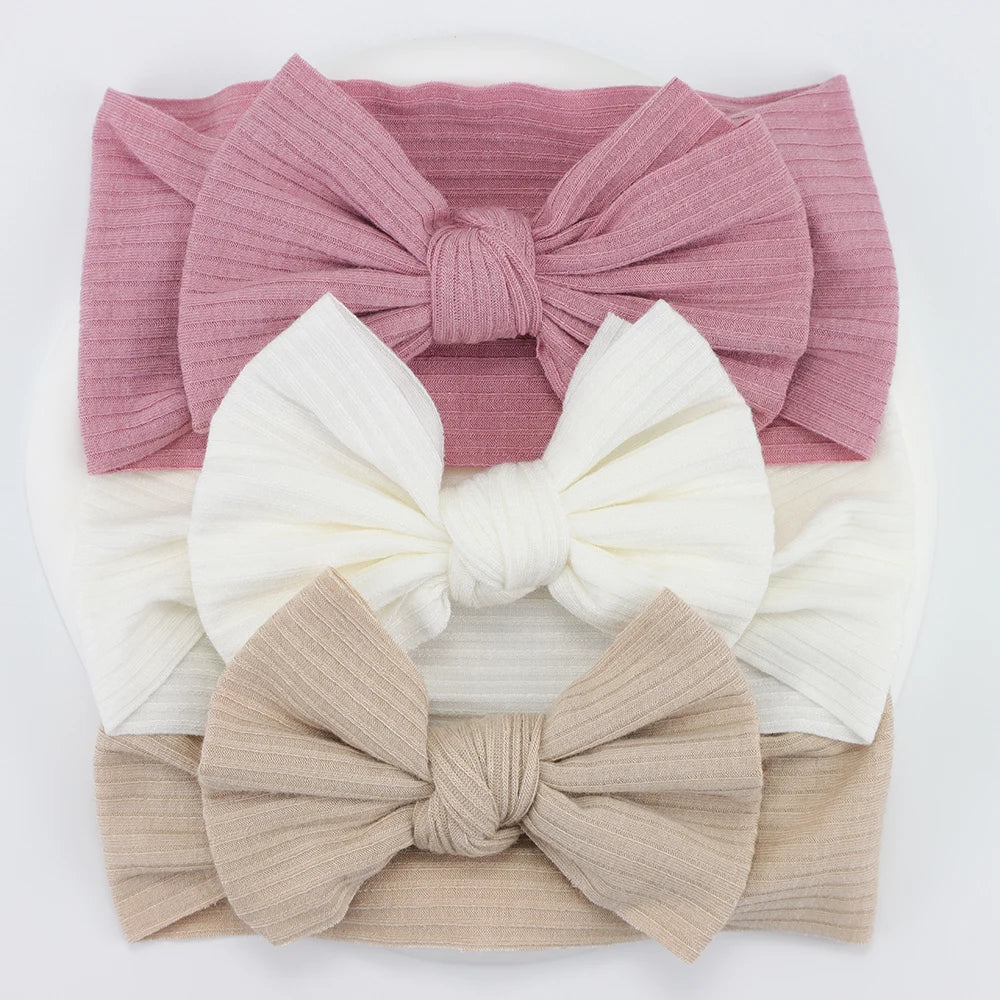Set of 3 soft, flexible nylon baby headbands with ribbed bows in pink, white, and beige.