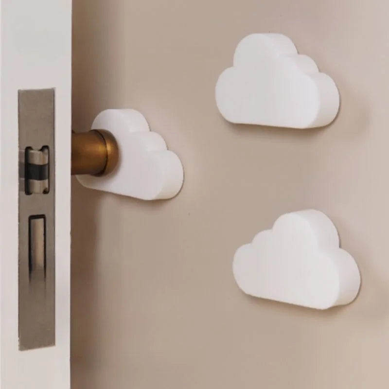White cloud-shaped silicone door stoppers and wall protectors, one on a door handle and two on a beige wall.