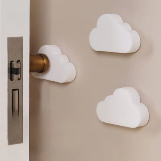 White cloud-shaped silicone door stoppers and wall protectors, one on a door handle and two on a beige wall.