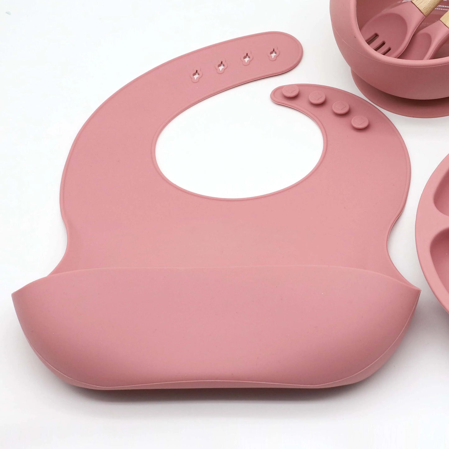 Pink silicone baby feeding set with adjustable bib, suction plate, and bowl.