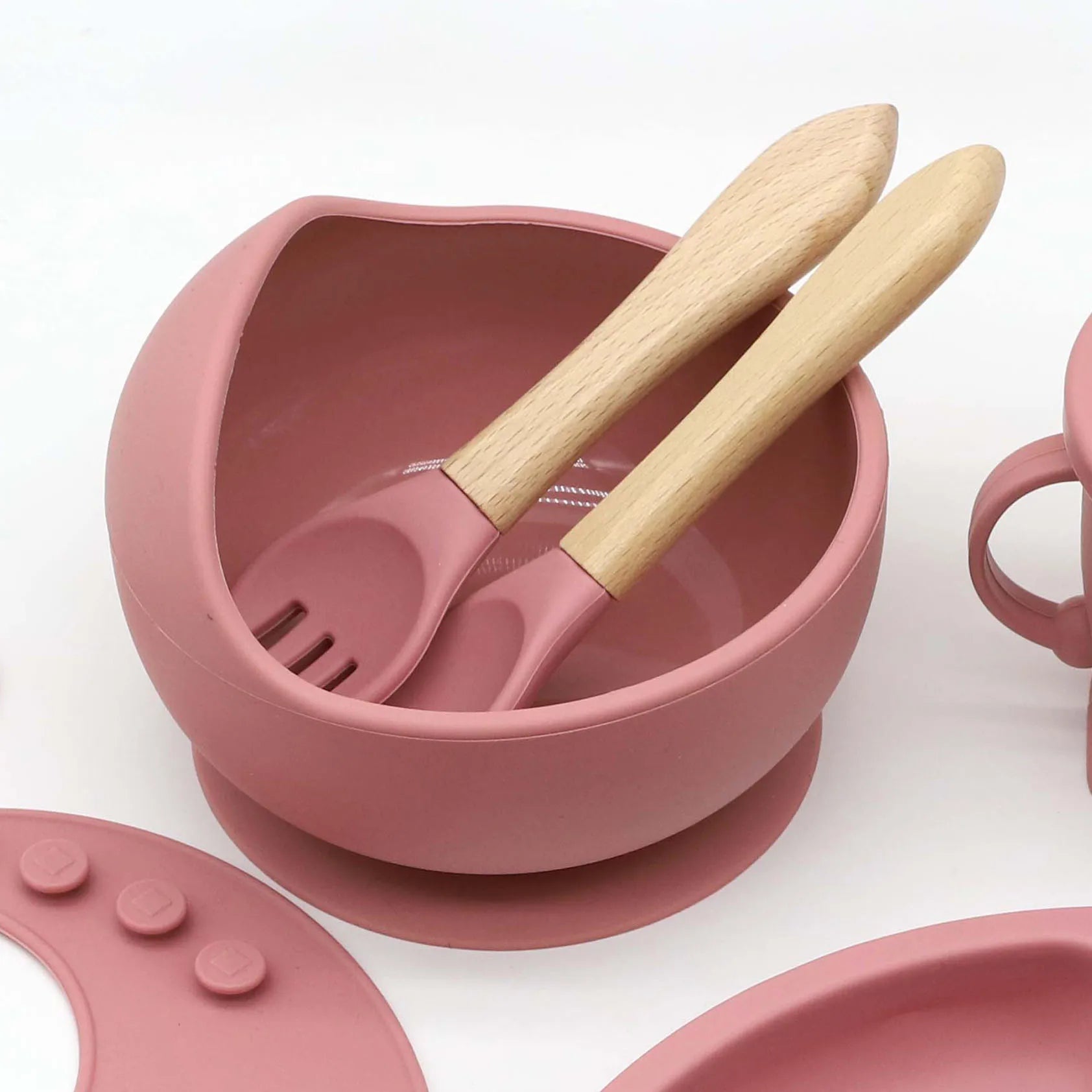 Pink silicone baby feeding set with suction bowl, wooden handle spoon, and fork.