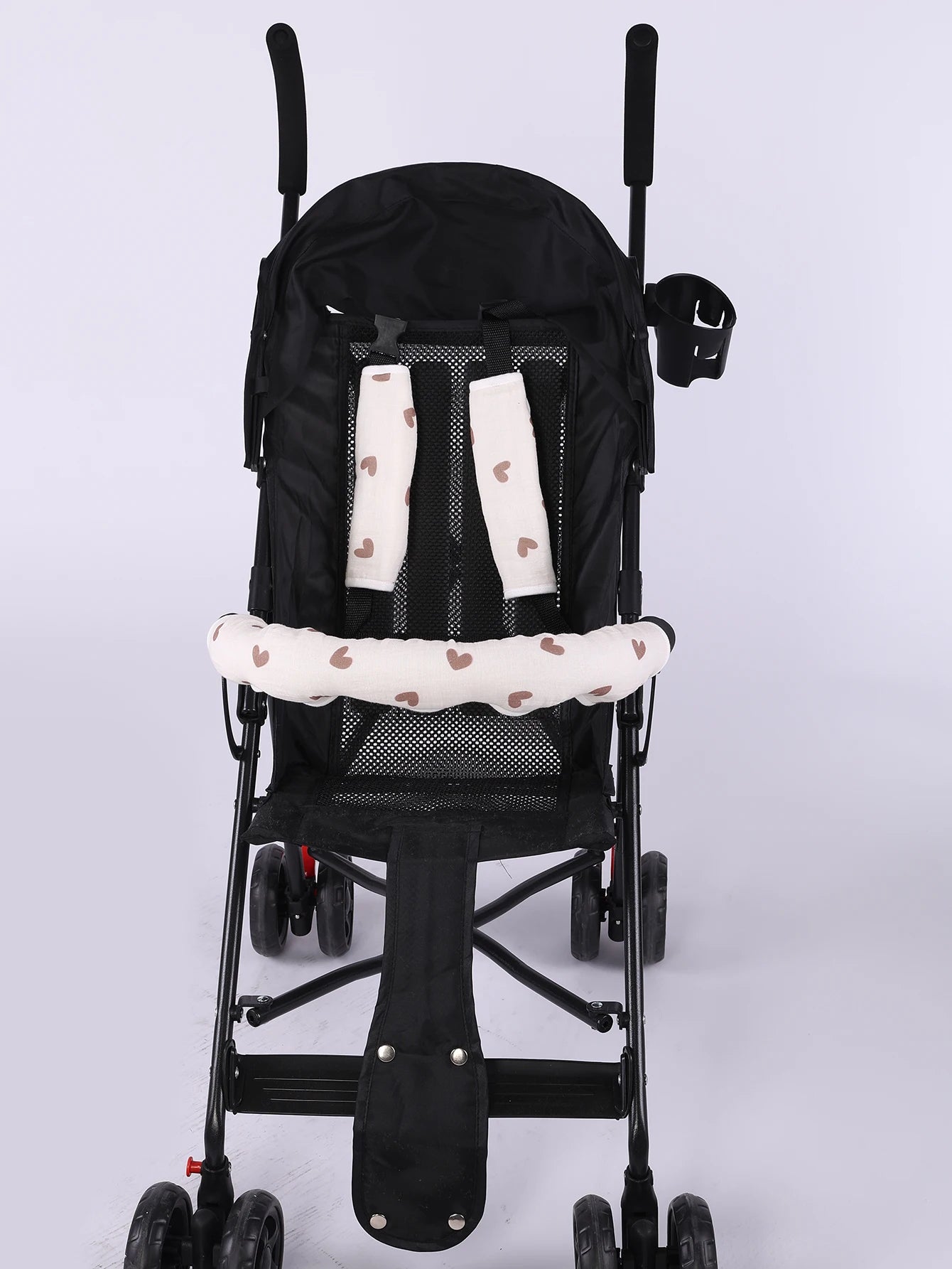 Beige heart-patterned stroller handle cover and safety belt pads on a black baby stroller.
