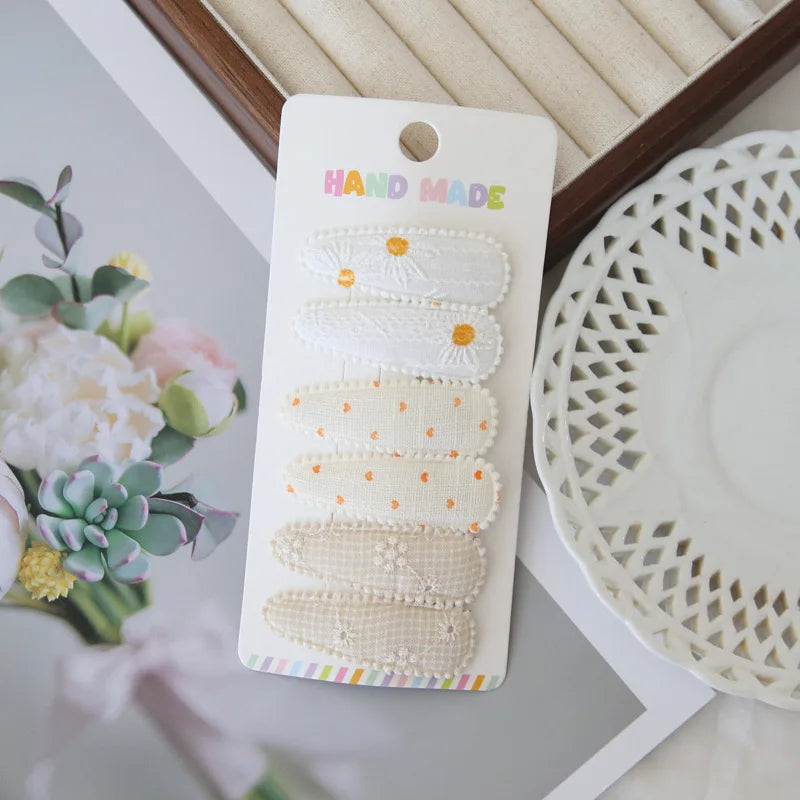 Set of 6 handmade white and beige floral snap hair clips for girls, featuring embroidered daisy and polka dot designs.
