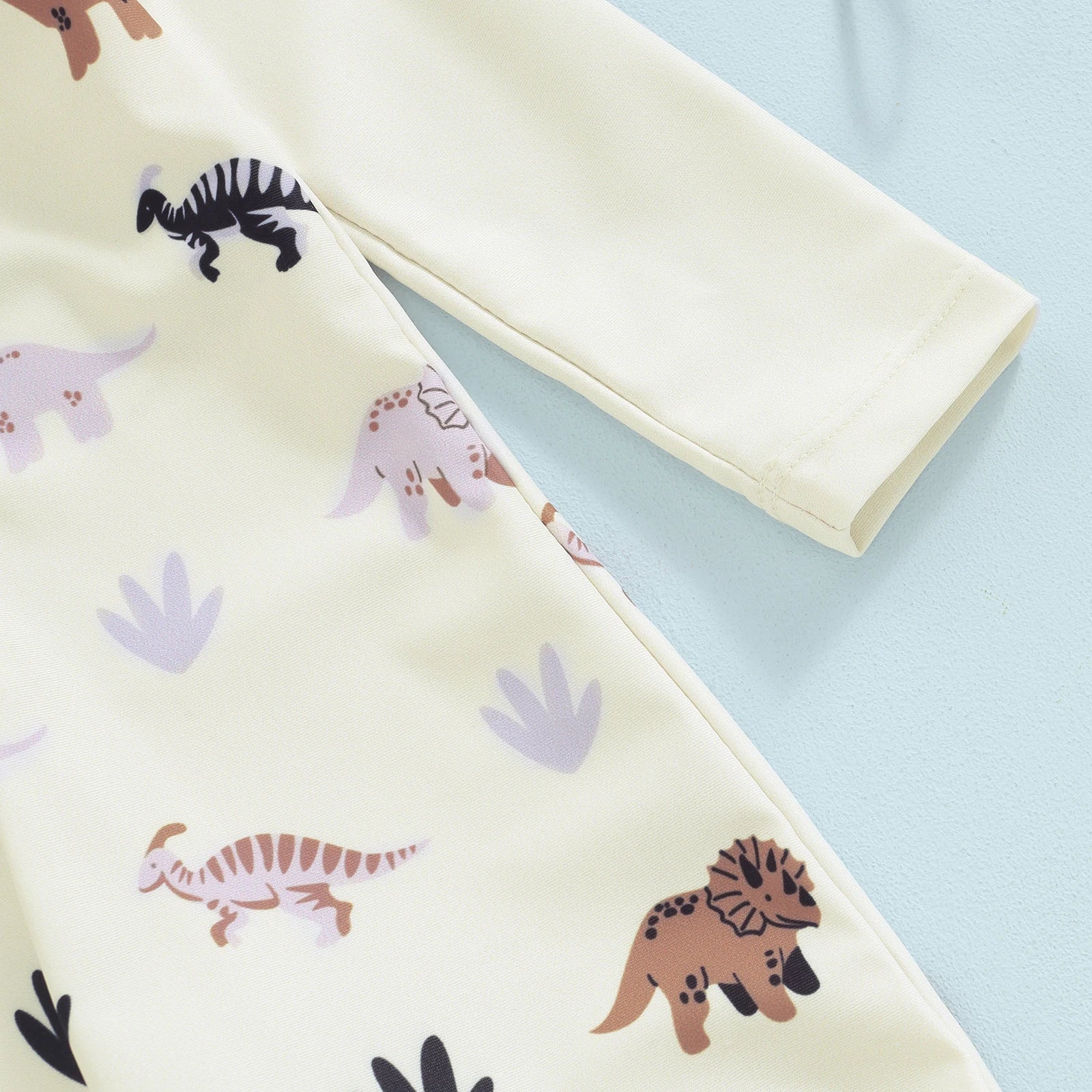 Cream long-sleeve baby swimsuit with colorful dinosaur print and matching sun hat.