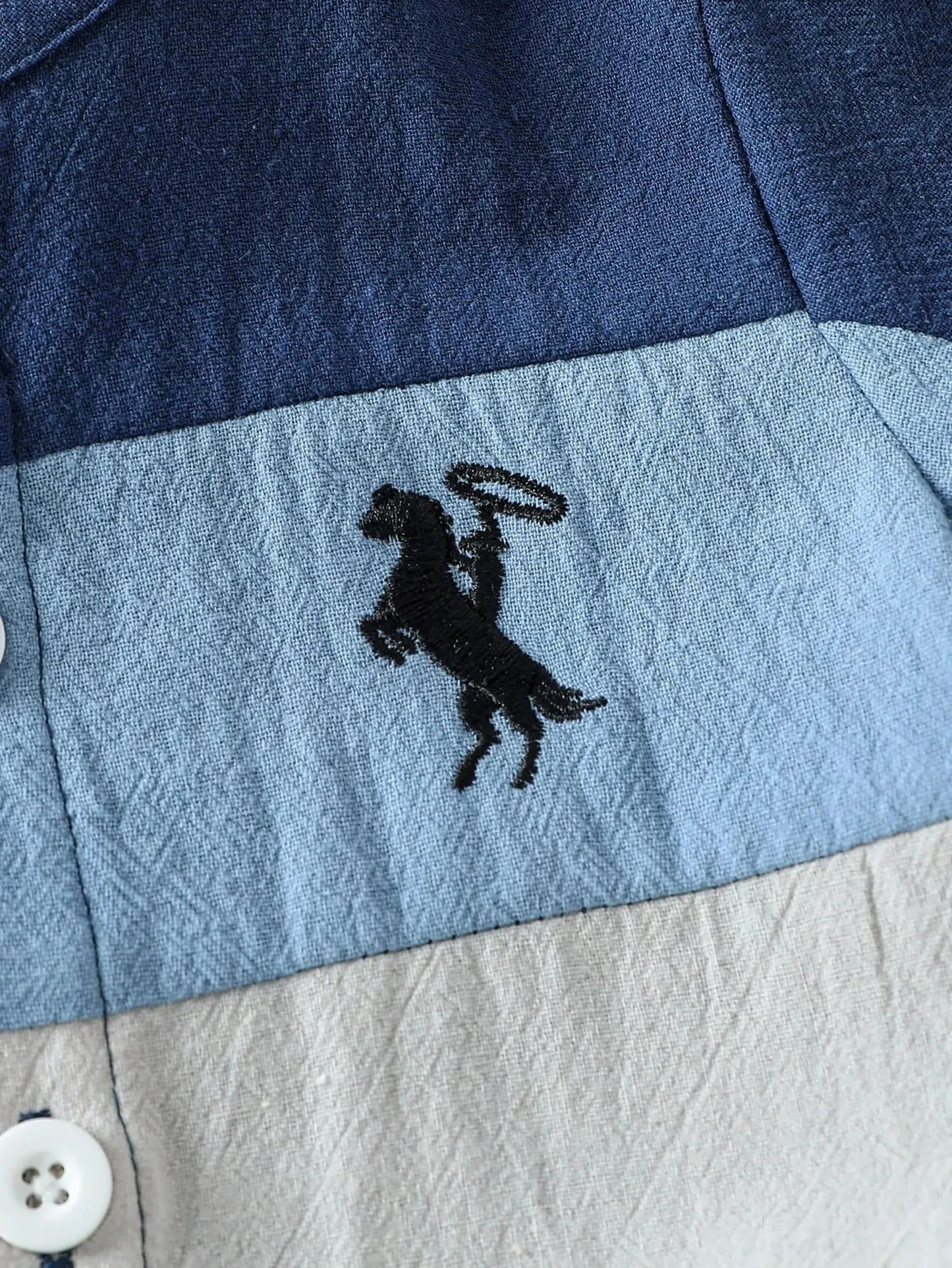 Close-up of a baby's cotton summer outfit with blue, light blue, and beige color blocks and a black horse embroidery.