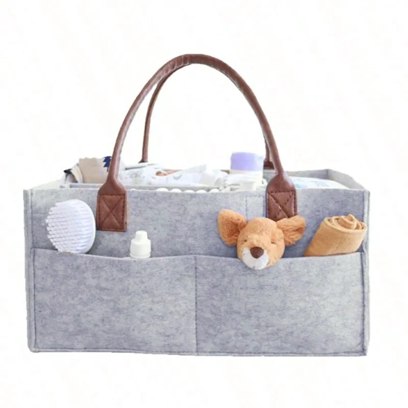 Gray felt baby diaper caddy with brown faux leather handles, multiple compartments, and baby items.
