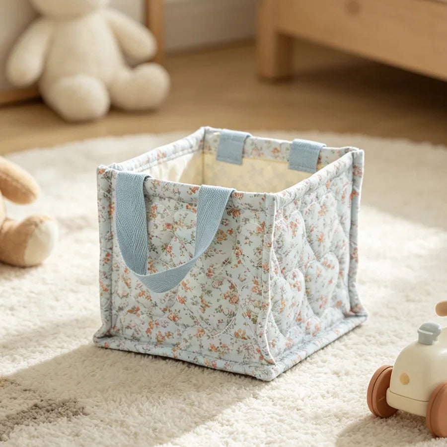 Square quilted polyester storage basket with delicate floral pattern and blue handles.