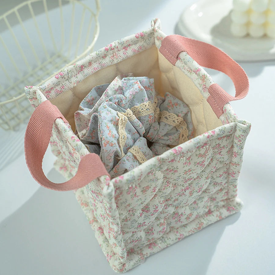 Quilted square storage basket with delicate pink floral print, pink handles, and light blue fabric inside.