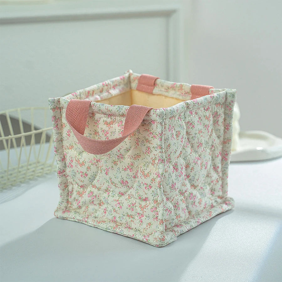 Square quilted polyester storage basket with delicate pink floral print and pink handles.