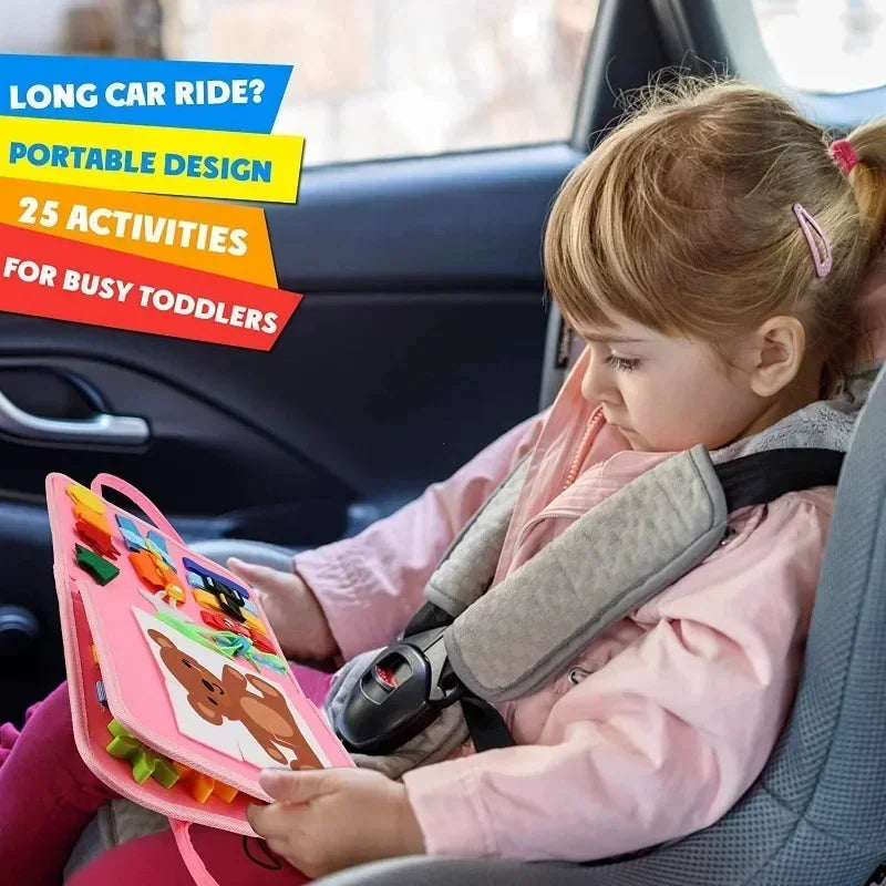 Toddler in car seat playing with a pink felt Montessori busy book featuring dinosaur and animal activities.