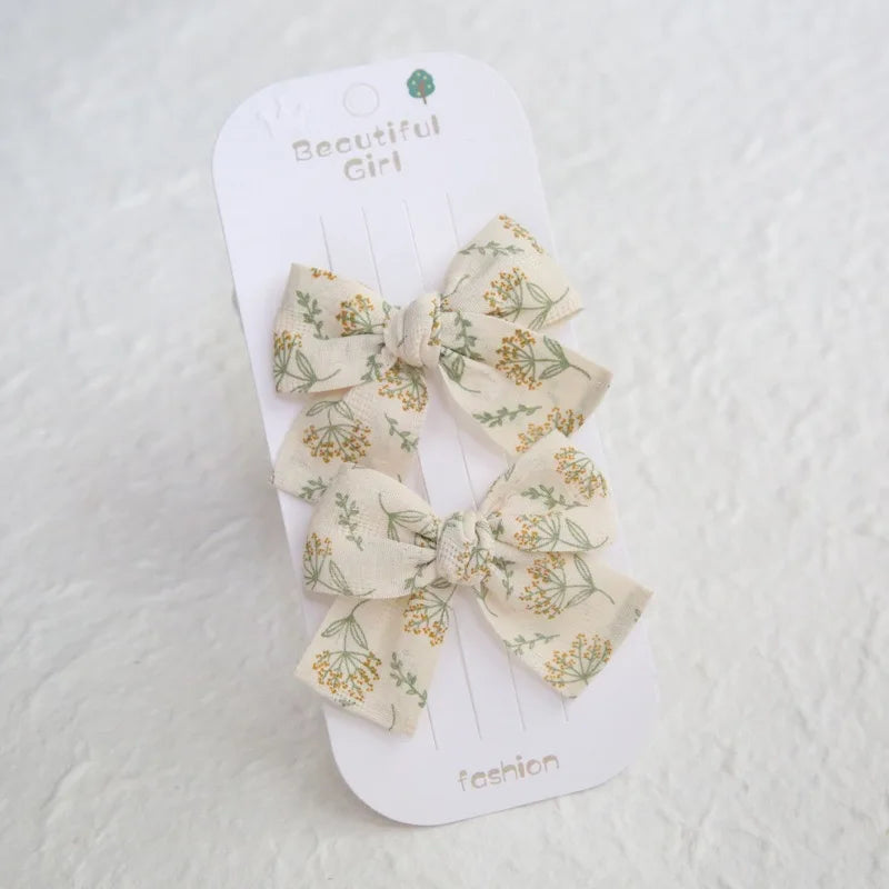 Two cream cotton hair bows with green and yellow floral print on a white "Beautiful Girl" card.