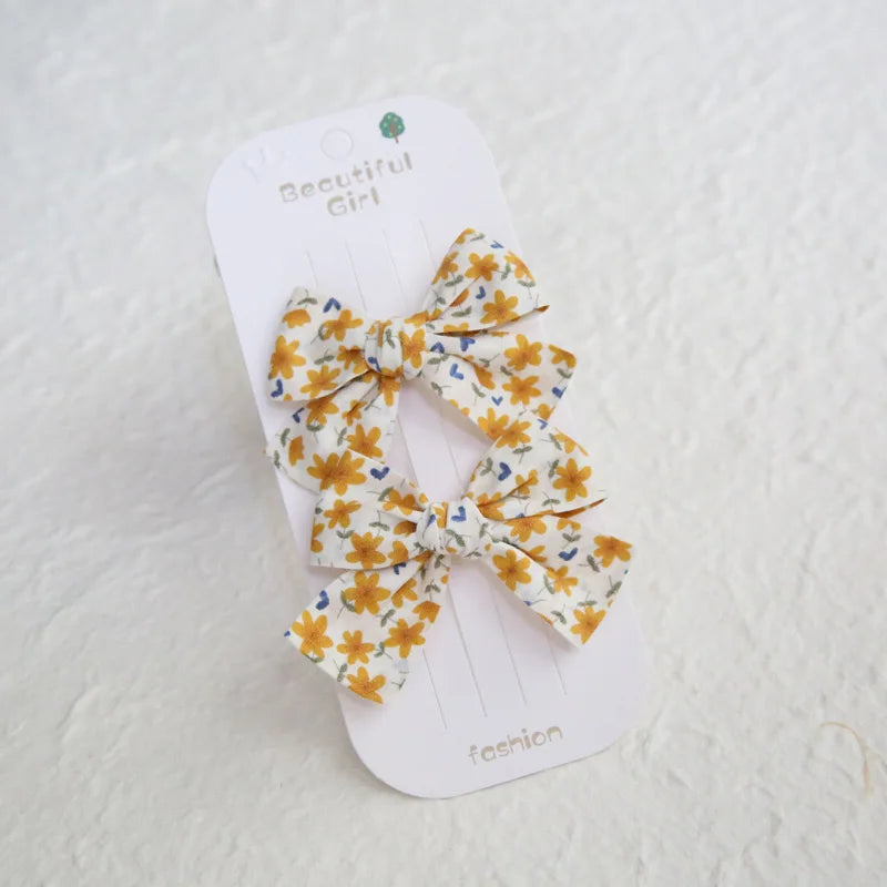 Two cotton hair clips with yellow floral bow design on a white card.