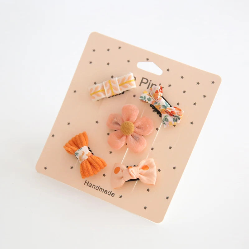 Set of five colorful fabric hair clips for babies, featuring bows and a flower design on a pink card.